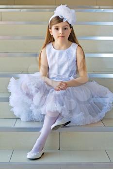 Nice little girl wearing white dress sitting on the steps
