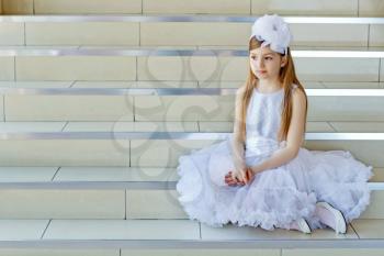 Pretty little girl in white dress sitting on the steps