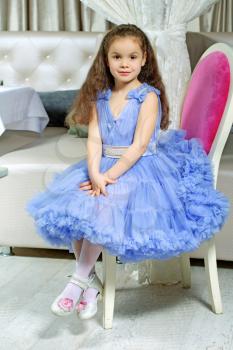 Curly little girl in blue dress sitting on the chair