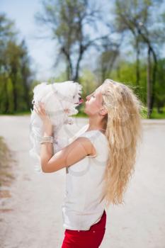 Curly blond woman kissing white dog in the park