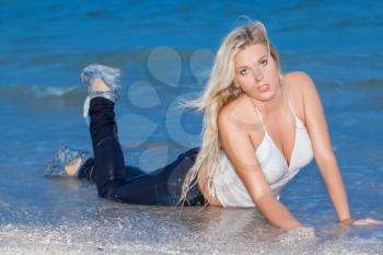 Sexy blonde in white shirt and wet jeans posing on the beach