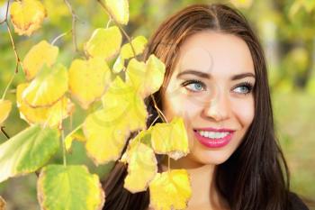 Portrait of smiling brunette posing behind yellow leaves