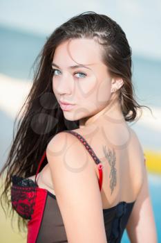 Portrait of alluring young brunette with tattoo posing on the beach in corset