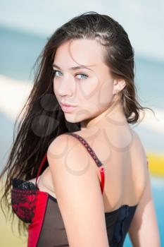 Portrait of alluring young brunette posing on the beach in corset