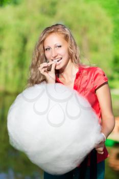 Joyful blond woman posing with a cotton candy outdoors