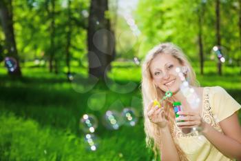 Portrait of cheerful blond woman blowing soap bubbles in the park