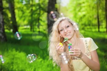 Portrait of pretty blonde blowing soap bubbles in the park