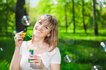 Portrait of cheerful young woman blowing bubbles in the park