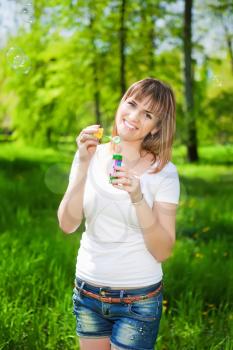 Portrait of young joyful woman blowing bubbles in the park