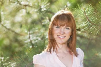 Smiling red-haired woman posing near the pine