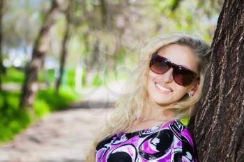 Portrait of pretty blond woman wearing sunglasses and posing near the tree