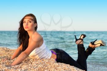 Thoughtful young brunette wearing jeans and shoes posing on the beach