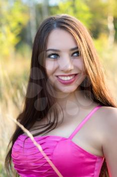 Portrait of young smiling brunette posing in pink dress