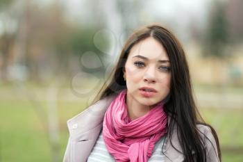 Portrait of young brunette with pink scarf posing outside