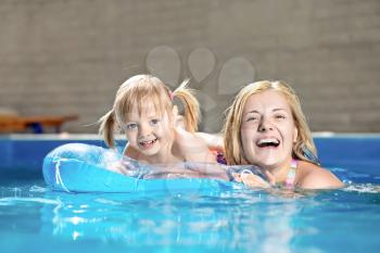 Attractive little girl and her mother swimming in water pool