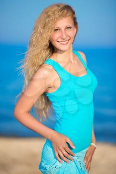 Cheerful curly blond woman in blue t-shirt posing on the beach