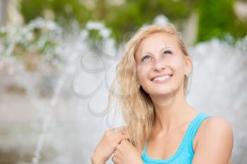 Portrait of pretty smiling blond woman posing near the fountain