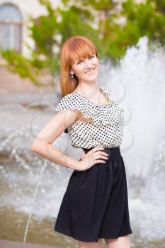 Pretty redhead woman posing near the fountain