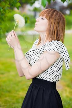 Pretty young redhead woman posing with dandelion