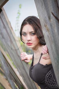 Pensive woman in gray dress posing behind the wooden fence