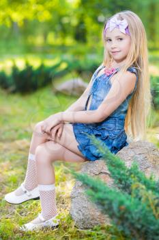 Beautiful little girl sitting on the stone outdoors
