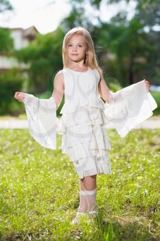Little blond girl showing her beautiful white dress outdoors