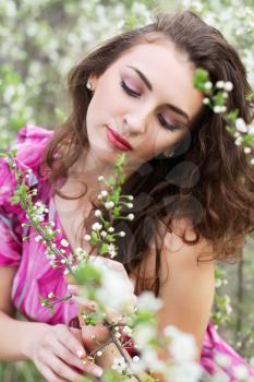 Portrait of young curly lady touching the branch of flowering tree