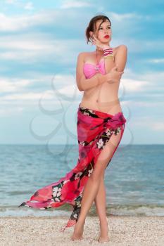 Beautiful young lady in pink bra and flowered pareo posing on the beach
