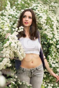 Pretty slim brunette wearing top and jeans posing in flowering bushes