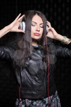 Young brunette posing with headphones and closed eyes. Isolated on black