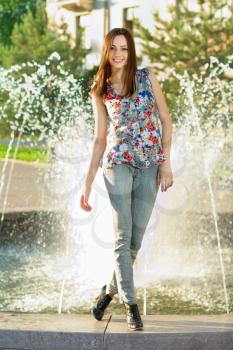 Pretty smiling brunette in flowered blouse posing near the fountain
