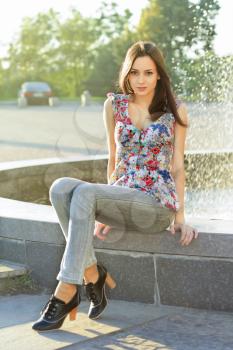 Attractive young lady in flowered blouse sitting by the fountain