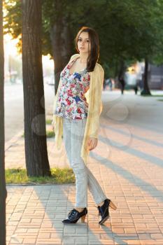 Pretty brunette in grey jeans and flowered blouse posing outdoors
