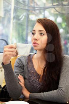 Young pensive woman drinking in a cozy cafe