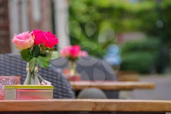Vase with beautiful roses, candle and decorative box on the tables of outdoor street cafe