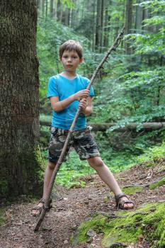 Boy with long wooden stick in forest park
