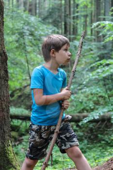 Boy with long wooden stick in forest park