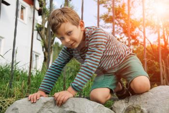 Small boy in striped sweater and shorts on big rocks in sunlight
