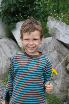 Smiling boy with dandelion in front of big rocks