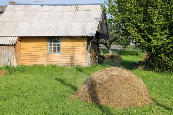 Haystack on green lawn in front of wooden house