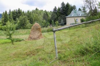 Haystack on green lawn near modern house on forested hill