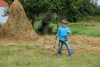 Boy with wooden sword near haystack on green lawn
