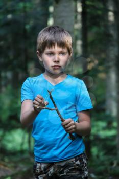 Handsome boy with makeshift slingshot in summer forest