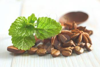Fresh spearmint leaves, wooden spoon with coffee grains and anise spice star on retro wooden table food background. Selective focus. Aroma spicy caffeine drink ingredients.