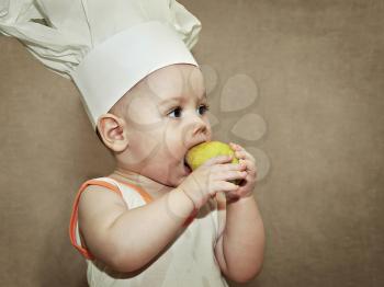 little baby in a chef's hat eating a pear