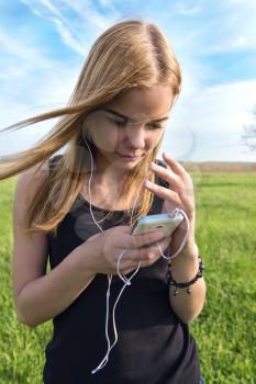 young blond woman listening to music with headphones outdoors