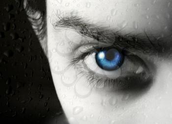 Photo of half of face of the beautiful young blue-eyed girl and drop of a rain on glass