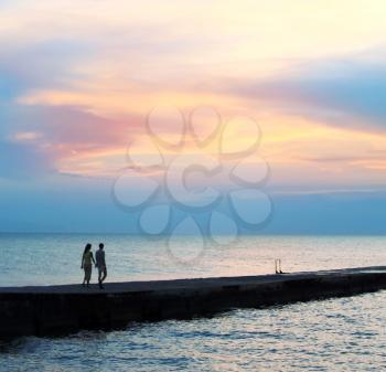 A couple in love goes on a breakwater against the background of a beautiful sunset