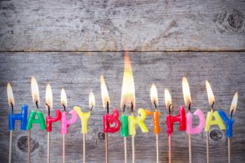Happy birthday candles burn against wooden background