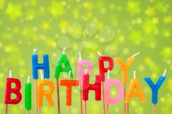 Colorful candles forming the sentence happy birthday on the green blurry background